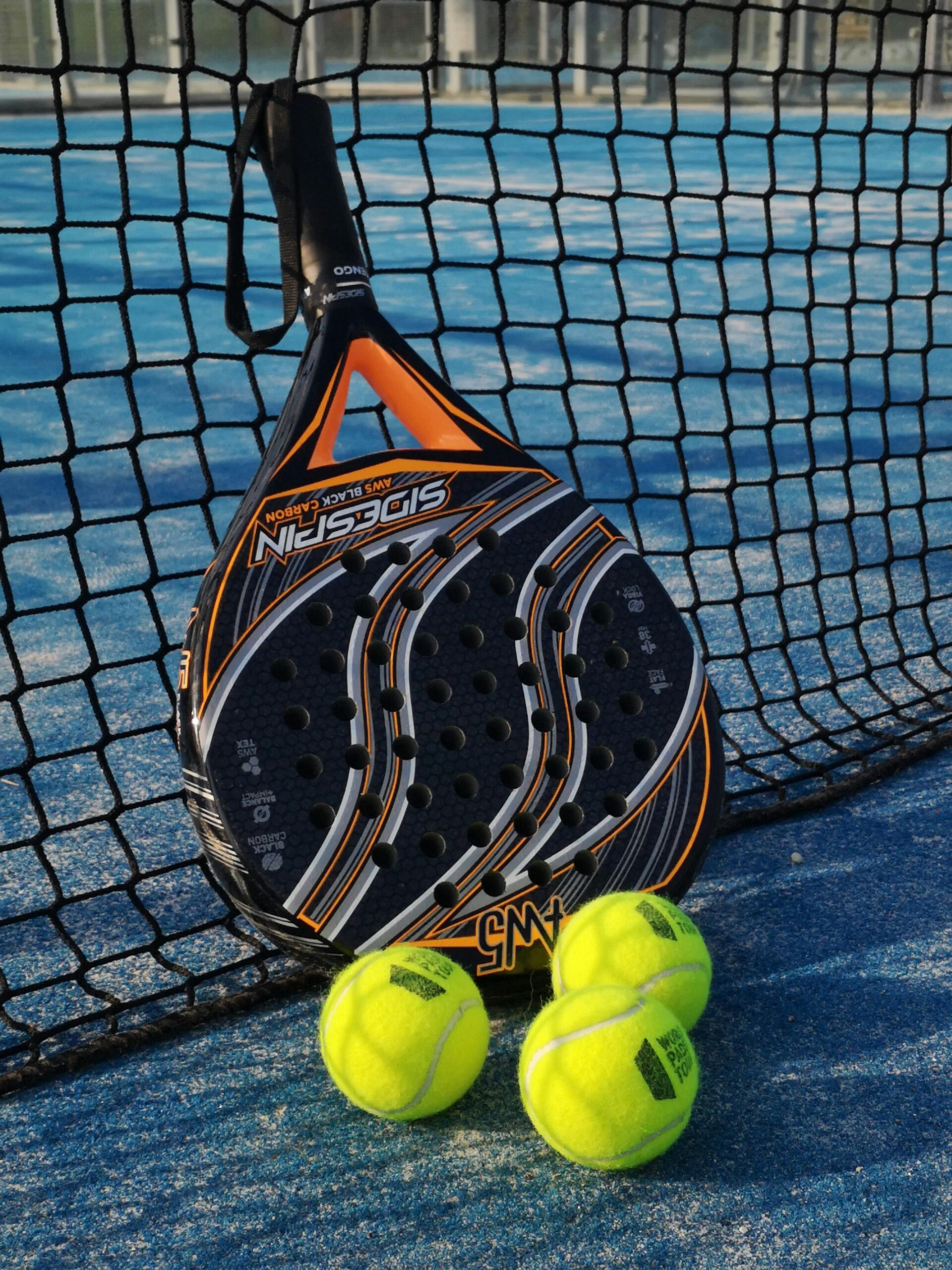 From above of padel racket and small colorful balls near fence on sports ground